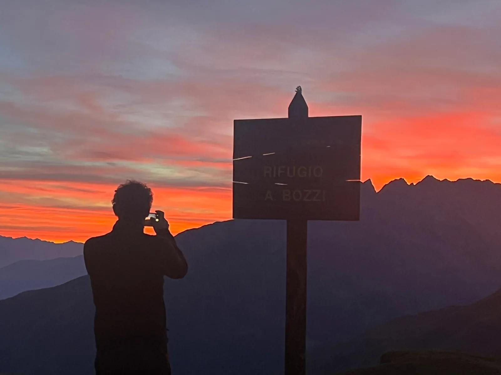 Tramonto infuocato dietro il cartello del Rifugio Bozzi